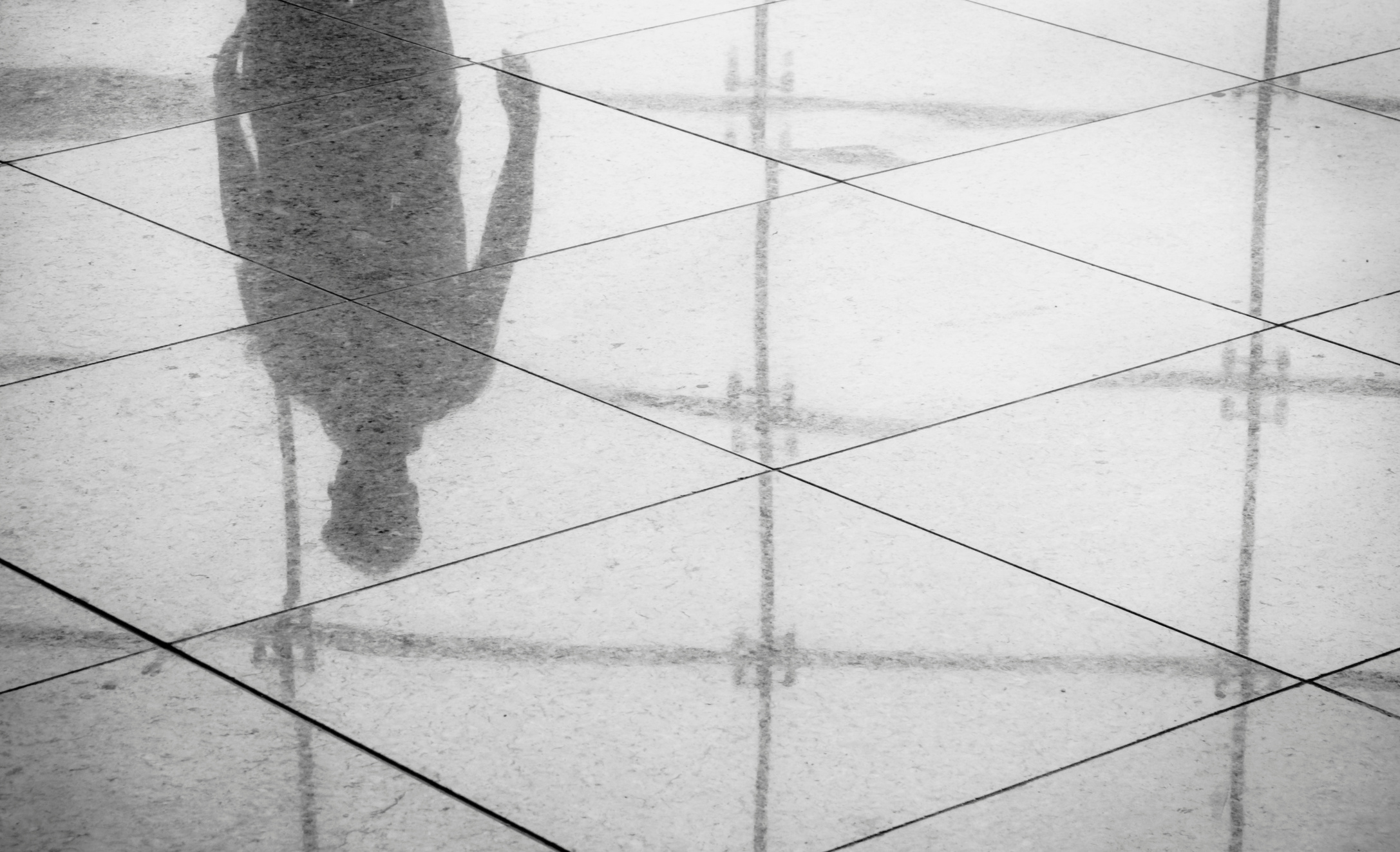 Man's reflection in lobby's shiny tile floor